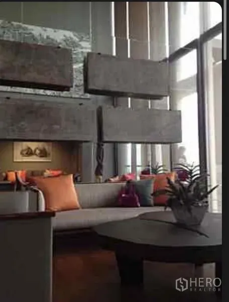 Condominium for rent in Sathon, Bangkok - Double-height living room with sofa, coffee table, decorative concrete panels and floor-to-ceiling windows.