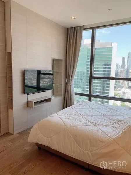 Condominium for sale - Bedroom with wall-mounted TV and panoramic city views through large windows.