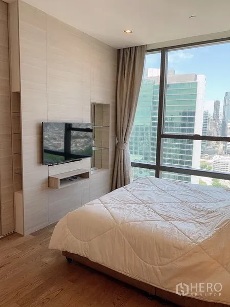 Condominium for sale - Bedroom with wall-mounted TV and panoramic city views through large windows.
