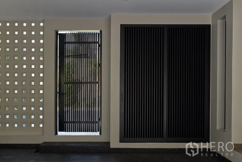 Detached House for rent in Watthana, Bangkok - Covered entrance with black slatted gate and breeze-block ventilation wall.