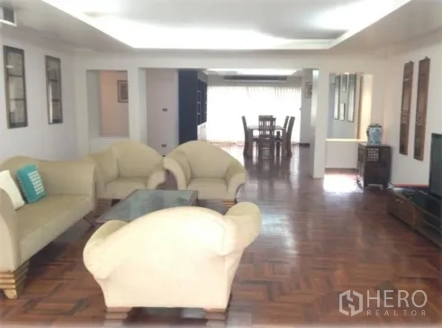 公寓 出租在Watthana, Bangkok - 大开间客厅，米色沙发、玻璃茶几与拼花地板，连通餐区。
