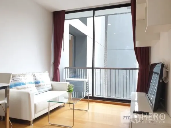 Condominium for rent or sale in Bang Rak, Bangkok - Living room with white sofa and glass coffee table opening to a balcony via large sliding doors.