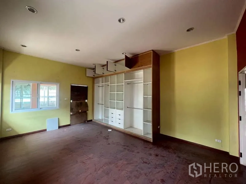 Detached House for rent in Watthana, Bangkok - Empty room with built-in white shelving and wood floors, yellow walls and a window.