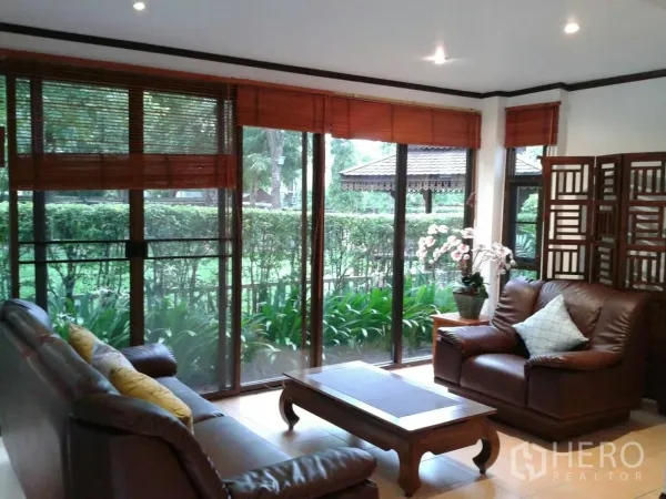 独立式住宅 出租在Suan Luang, Bangkok - 明亮客厅，皮沙发与落地窗，眺望修剪整齐的花园。