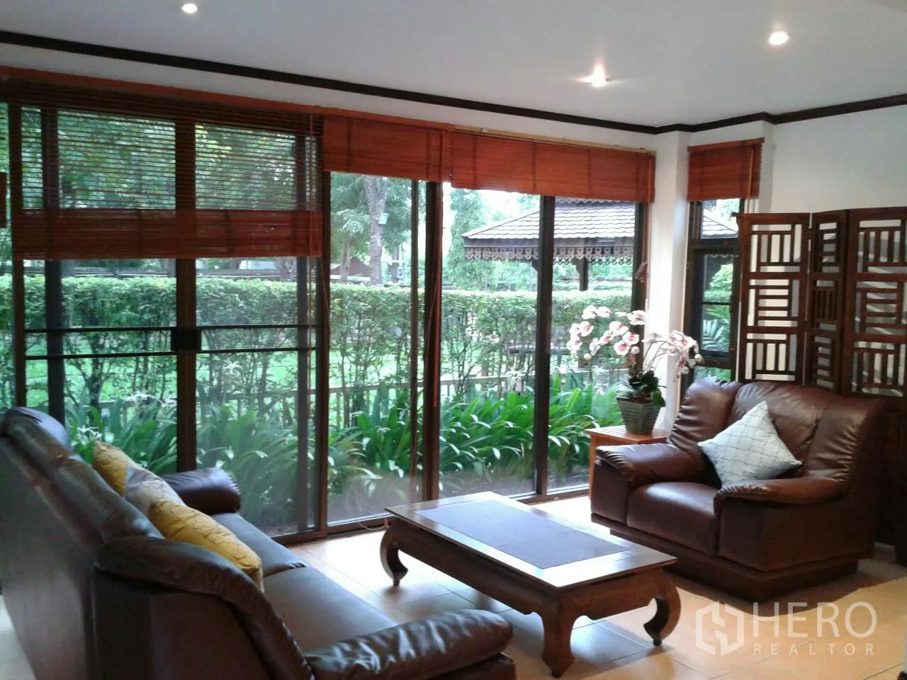 独立式住宅 出租在Suan Luang, Bangkok - 明亮客厅，皮沙发与落地窗，眺望修剪整齐的花园。