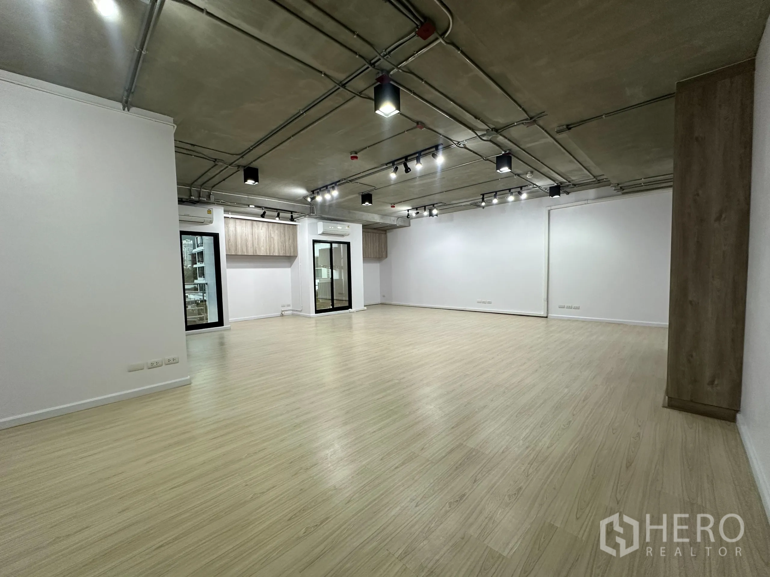 办公空间 出租在Watthana, Bangkok - 开放式办公区，浅木色地板，外露天花与轨道灯，滑动玻璃门与壁柜。