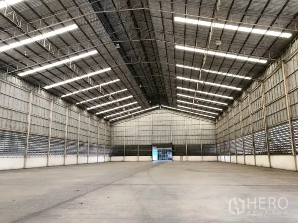 Warehouse for rent in Phra Nakhon Si Ayutthaya - Expansive warehouse interior with a high steel truss roof, bright strip lights, and open concrete floor.