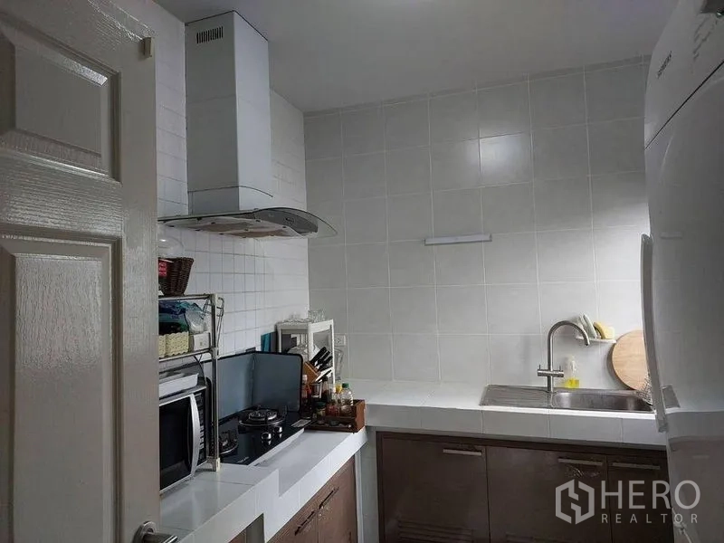 独立式住宅 出售在Khlong Sam Wa, Bangkok - 紧凑泰式厨房，白色台面，灶台与抽油烟机，水槽齐全。
