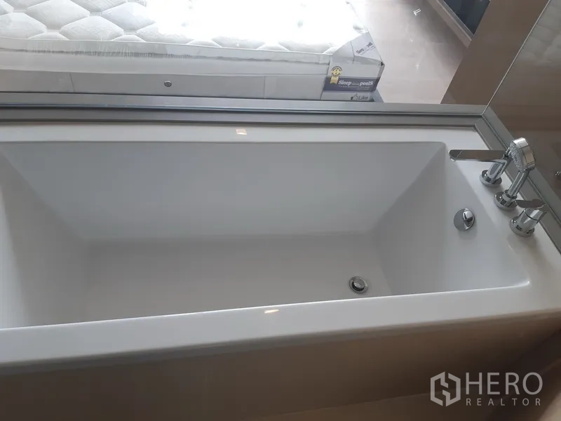Condominium for rent or sale in Watthana, Bangkok - Deep soaking bathtub beside bedroom window with city outlook.