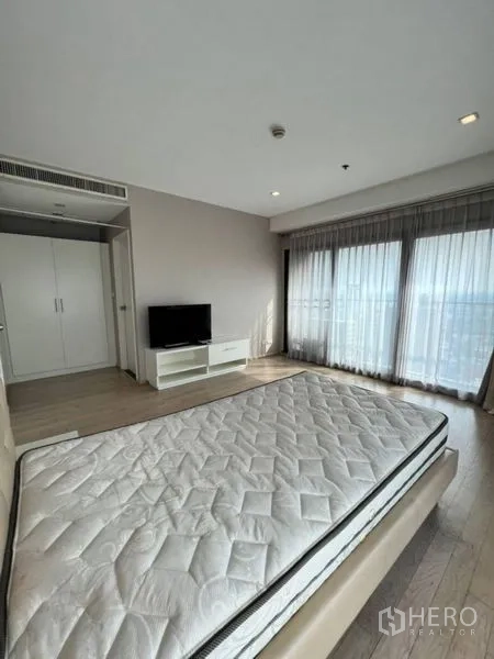 Condominium for rent in Khlong Toei, Bangkok - Master bedroom with corner windows, balcony access, TV stand and wardrobe.