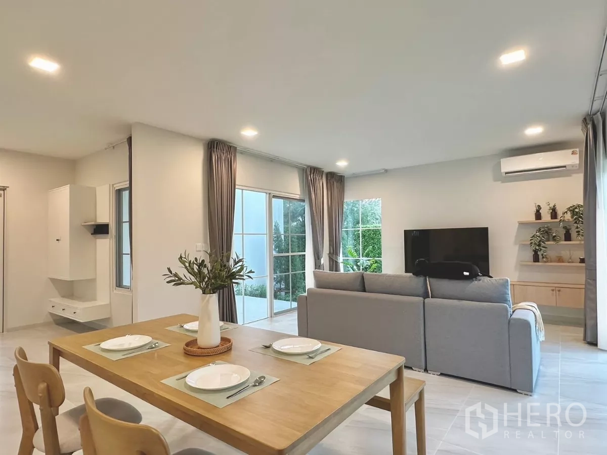 Detached House for rent in Bang Phli, Samut Prakan - Dining table for four facing a TV wall with shelves and garden views through windows.