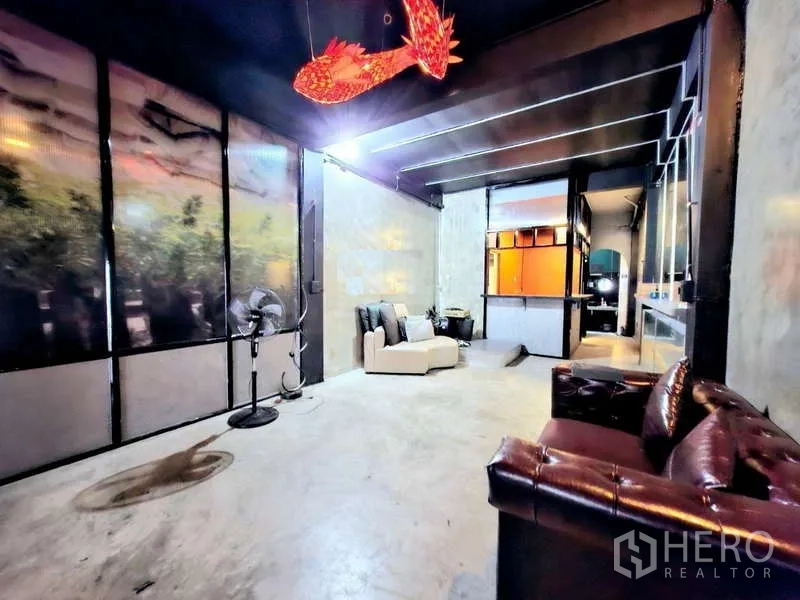 店屋 出租在Bang Rak, Bangkok - 一层工业风大厅，水泥地面、皮质沙发与红色鱼形吊灯。