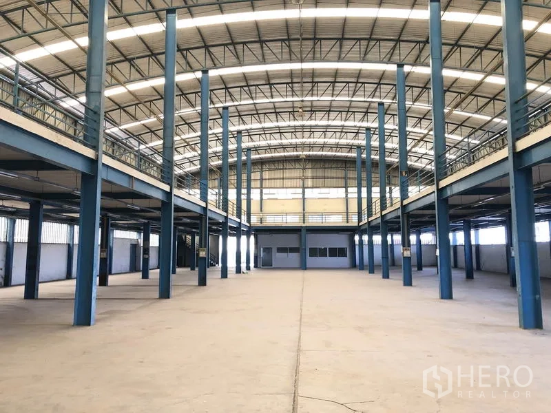 Factory for rent in Sai Noi, Nonthaburi - Spacious production hall with high arched roof, blue steel columns and dual-side mezzanine platforms.