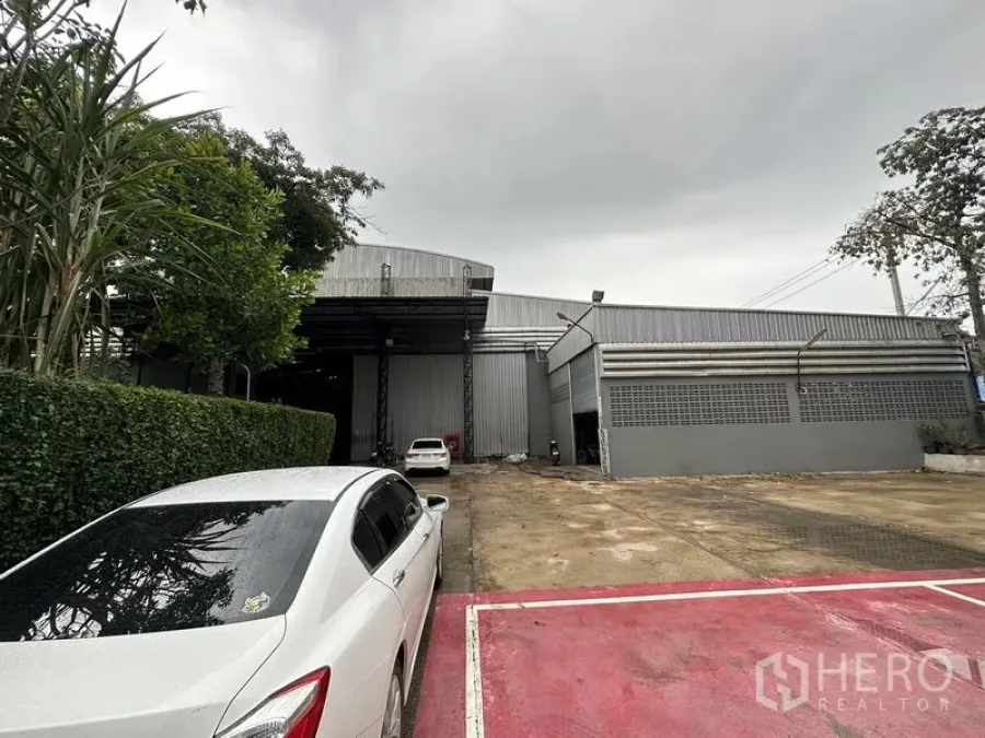 Factory for rent in Bang Bua Thong, Nonthaburi - Front facade of a metal-clad factory with a wide driveway and parking area.