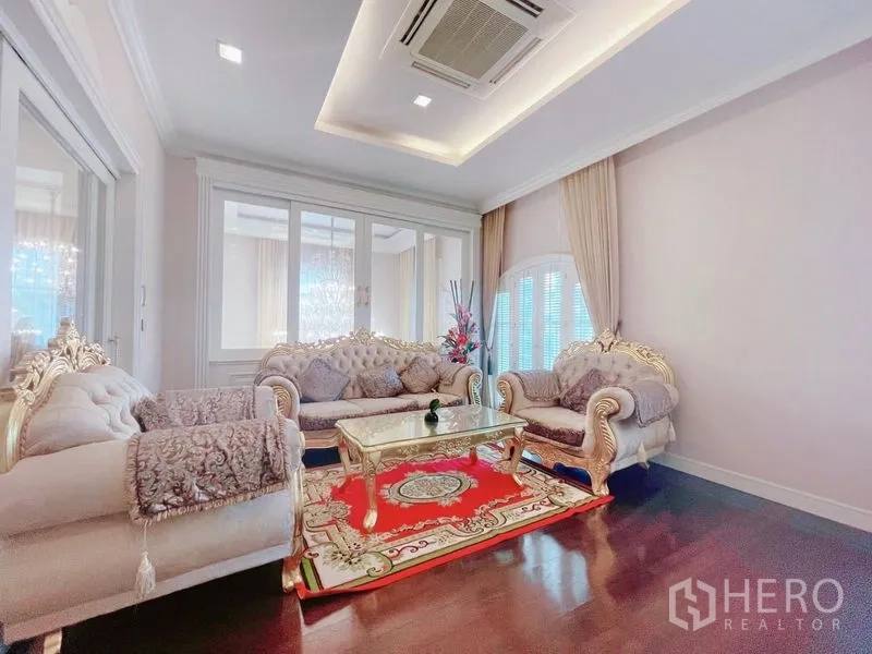 Detached House for rent or sale in Bang Phli, Samut Prakan - Classic living room with ornate sofas, glass coffee table, red rug, and tray ceiling.