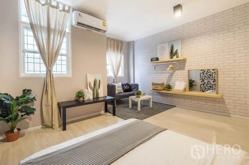 Detached House for rent in Khlong Toei, Bangkok - Neutral-toned bedroom with white brick wall, AC, sofa set and floating shelves.