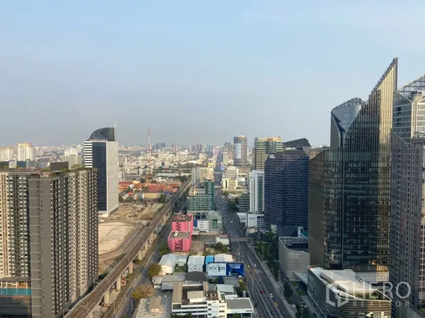 公寓 出租在Ratchathewi, Bangkok - 高楼层俯瞰曼谷天际线，可见轨道线与玻璃写字楼，天空晴朗。