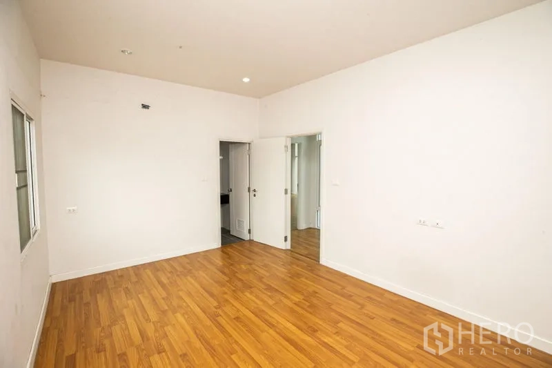 Detached House for rent or sale in Lam Luk Ka, Pathum Thani - Bedroom with wood floors, white walls and a door to an ensuite bathroom.