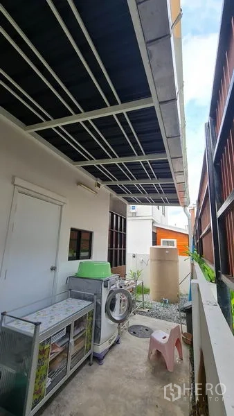 Detached House for sale in Samut Prakan - Covered side utility area with washing machine and storage beside the house.