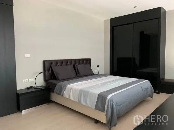 Condominium for rent in Khlong Toei, Bangkok - Spacious bedroom with upholstered bed, bedside tables, and glossy black wardrobe.