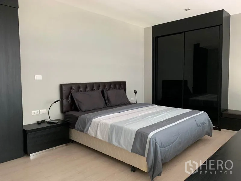 Condominium for rent in Khlong Toei, Bangkok - Spacious bedroom with upholstered bed, bedside tables, and glossy black wardrobe.