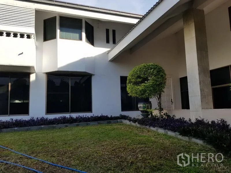 บ้าน ให้เช่าหรือขายในSuan Luang, Bangkok - บ้านเดี่ยวสองชั้นสีขาว หน้าต่างบานใหญ่ เฉลียงมีเสา และสนามหญ้าพร้อมพุ่มไม้ตัดแต่งทรงกลม