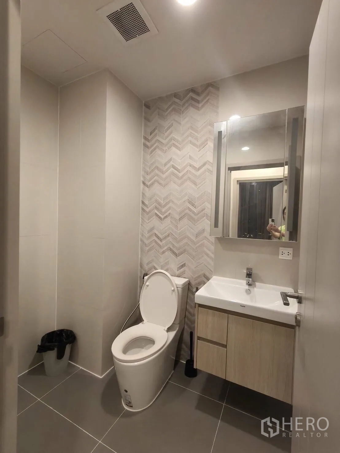 Condominium for rent in Khlong Toei, Bangkok - Second bathroom with a chevron accent wall, vanity with mirror, and toilet.