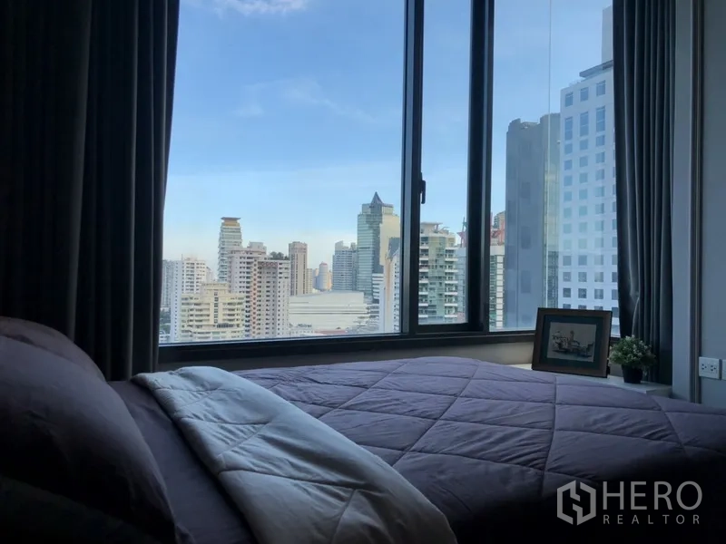 公寓 出租在Watthana, Bangkok - 卧室配大转角窗，俯瞰曼谷城市天际线，搭配灰色窗帘。
