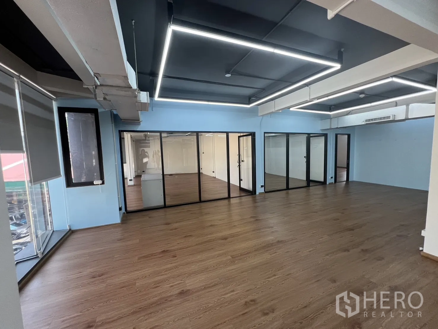 Office Space for rent in Khlong Toei, Bangkok - Open-plan office with wood floors, blue accent walls, glass-partitioned rooms and linear LED lighting.