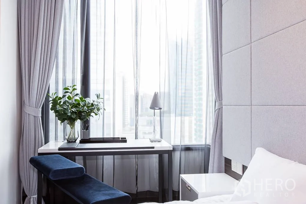 公寓 出租在Watthana, Bangkok - 卧室窗边书桌，灰色窗帘，远眺城市天际线。