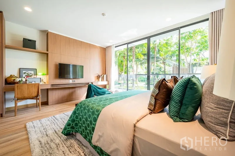 Condominium for sale - Garden-view bedroom with floor-to-ceiling glass, built-in desk and wall-mounted TV.