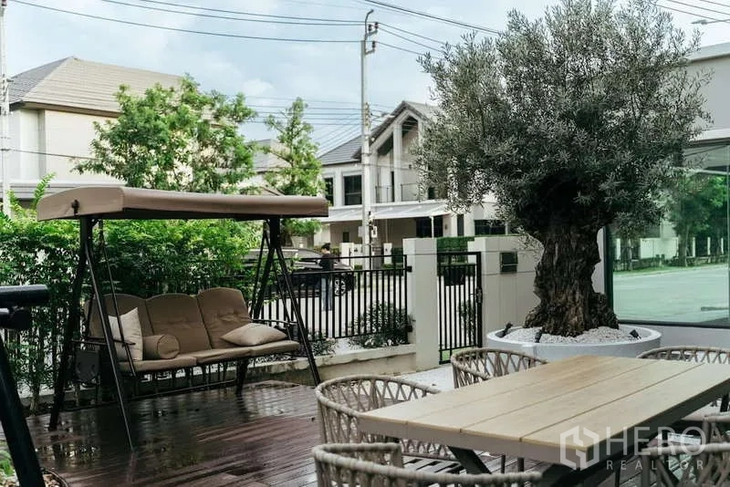 Detached House for sale in Sai Mai, Bangkok - Outdoor patio with swing seat, dining set and a mature potted tree beside the fence.
