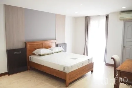 Condominium for rent in Pathum Wan, Bangkok - Second bedroom with wooden bedframe, bedside units and tall windows.