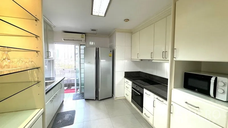 Condominium for rent or sale in Watthana, Bangkok - Kitchen view showing built-in oven, cooktop, microwave, and access to the balcony.