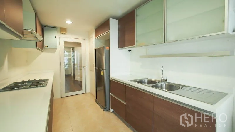 Condominium for rent in Khlong San, Bangkok - Modern galley kitchen with twin sinks, ample cabinetry, and stainless refrigerator.