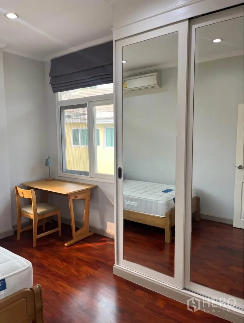 Detached House for rent or sale in Lat Phrao, Bangkok - Bedroom featuring mirrored sliding wardrobe, desk and air conditioner.