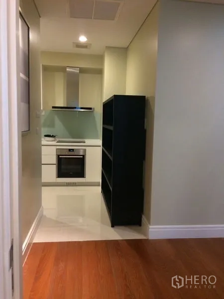 Condominium for rent in Khlong Toei, Bangkok - Modern compact kitchen with white cabinetry, built-in oven, range hood, and glossy backsplash.