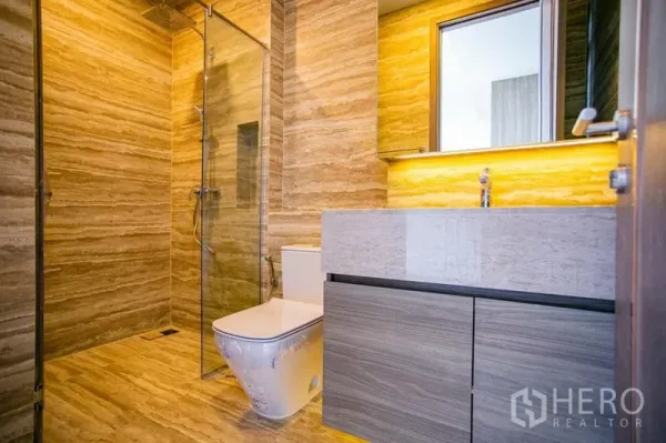 Condominium for rent in Watthana, Bangkok - Modern bathroom with glass shower, stone tiles, and backlit vanity.