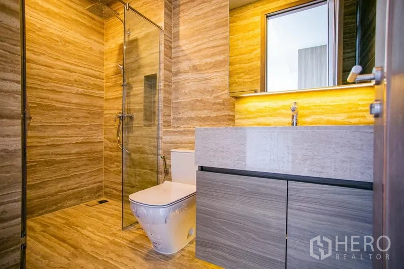 Condominium for rent in Watthana, Bangkok - Modern bathroom with glass shower, stone tiles, and backlit vanity.