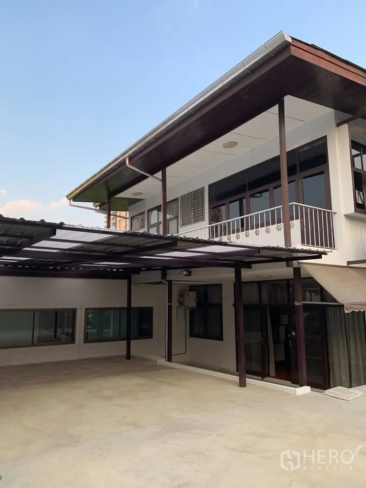 Detached House for rent in Phra Khanong, Bangkok - Two-storey house exterior with balcony and large covered carport in paved courtyard.