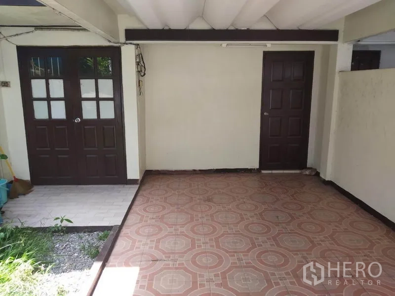 联排别墅 出租或出售在Wang Thonglang, Bangkok - 住宅前有顶庭院/车棚，花纹地砖与两扇深色木门。