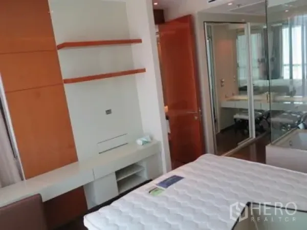 Condominium for rent in Khlong Toei, Bangkok - Bedroom with built-in shelves, work desk, and mirrored wardrobe beside the ensuite entrance.