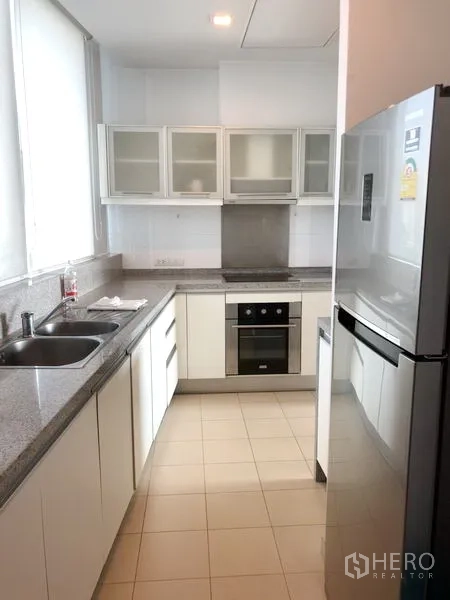 Condominium for rent in Khlong Toei, Bangkok - Galley kitchen with white cabinetry, granite countertops, built-in oven and large refrigerator.