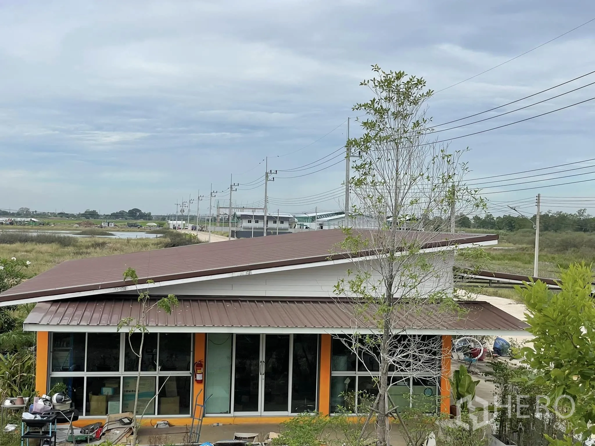 Warehouse for rent or sale in Pathum Thani - Rooftop perspective over a brown metal-roof building and access road with power lines.
