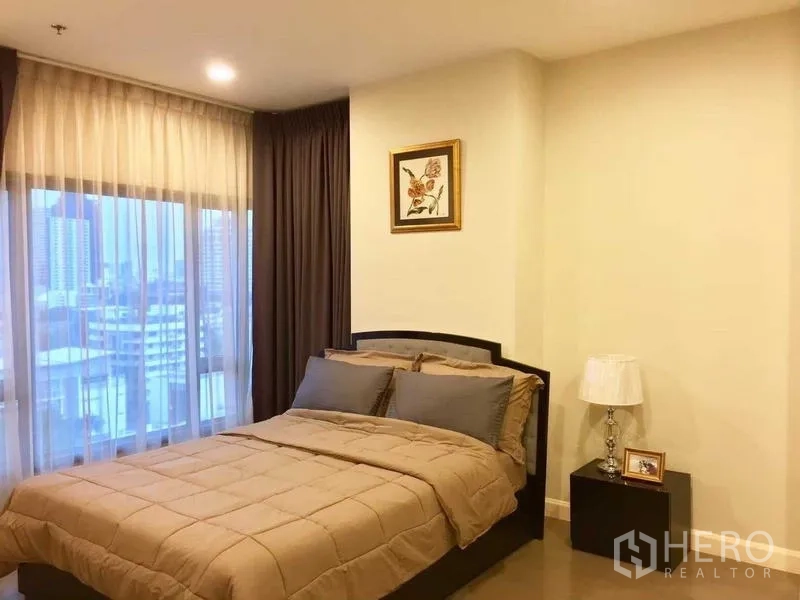 Condominium for rent in Khlong Toei, Bangkok - Master bedroom with large window, city view and a queen bed with neutral bedding.