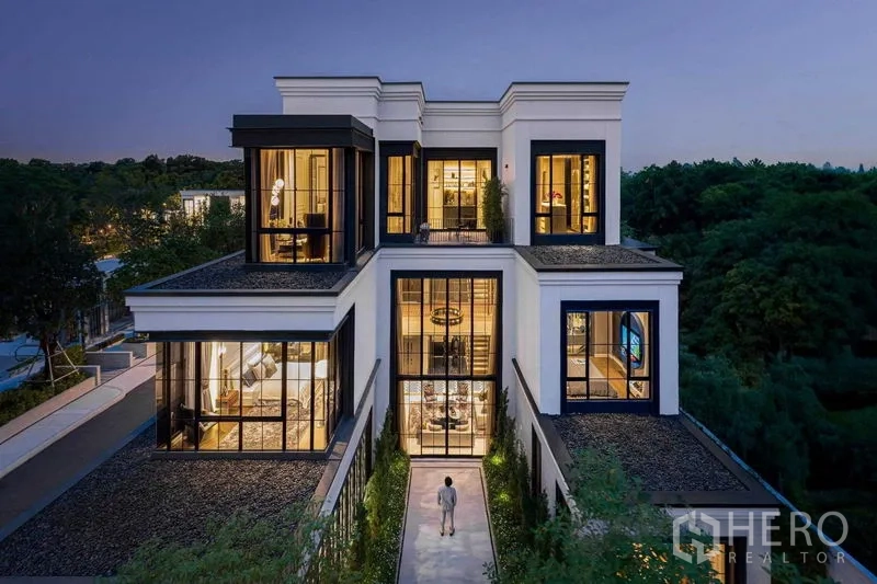 Detached House for sale in Saphan Sung, Bangkok - Contemporary three-storey detached house facade at dusk with floor-to-ceiling windows and landscaped walkway.