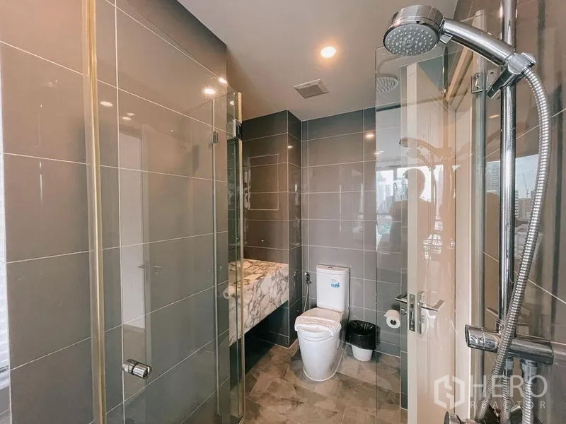 Condominium for rent in Ratchathewi, Bangkok - Sleek bathroom with glass shower, toilet and marble vanity.