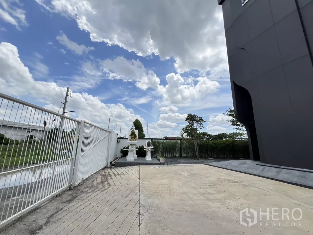 货栈 出售在Lat Krabang, Bangkok - 前方车道、推拉大门与院内神龛，蓝天白云。