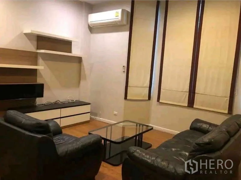 Townhouse for rent in Phra Khanong, Bangkok - Living room with leather sofas, glass coffee table, TV console and air conditioner.