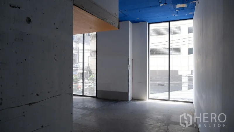 Retail Space for rent in Watthana, Bangkok - Empty retail interior with concrete floor, high blue ceiling, and floor-to-ceiling windows bringing natural light.